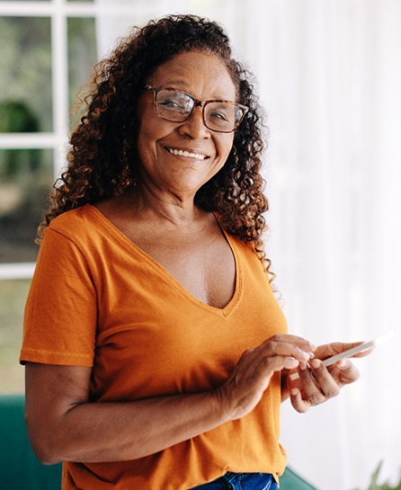 Senior woman with glasses smiling while looking at phone